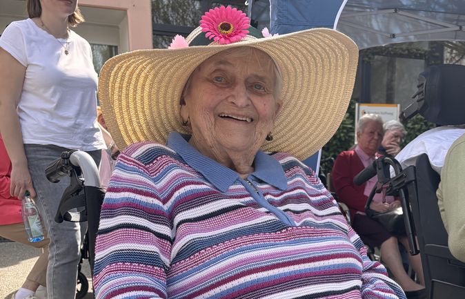Lächelnde ältere Frau im Rollstuhl mit Blumenhut auf Maifest